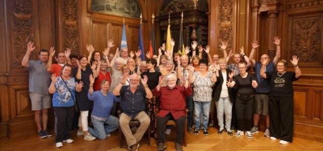 Bürgermeisterin Stefanie Jansen steht mit Vertreterinnen und Vertretern der beiden Gehörlosenvereine im Großen Rathaussaal. Alle heben die Hände nach oben und lächeln.