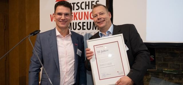 Marc Massoth überreicht Hans-Georg Böcher eine Urkunde zum 25-jährigen Bestehen des Verpackungsmuseums.
