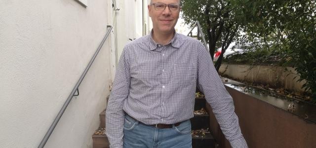 Jan Kotulla steht auf einer Treppe vor dem Haus der Wirtschaftsförderung und lächelt in die Kamera.