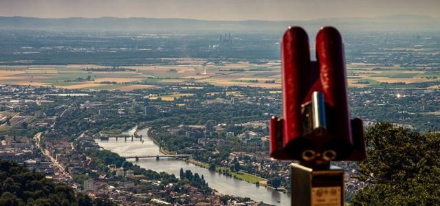 Im Vordergrund ein rotes Fernglas, im Hintergrund Heidelberg und der Neckar von oben.