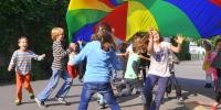 Schülerinnen und Schüler der Pestalozzischule spielen mit einem riesigen, bunten Schwungtuch in Regenbogenfarben 