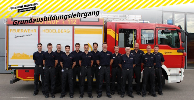 Grundausbildungslehrgang 2026 Gruppenbild der Lehrgangsteilnehmer und Ausbilder. Im Hintergrund ist ein Feuerwehrfahrzeug zu sehen