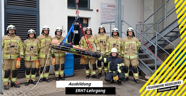 Absturzsicherung Gruppenbild der Lehrgangsteilnehmer. In der Mitte hängt eine an Seilen gesicherte Rettungstrage, in der eine Übungspuppe liegt.