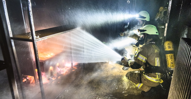 Atemschutzübung (Foto: Feuerwehr Heidelberg) Flammenschein über dem Helm eines Feuerwehrmanns bei einer Übung