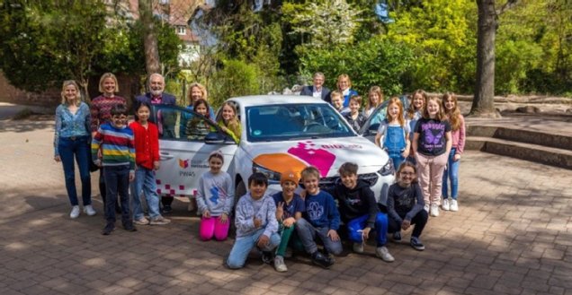 Mobiles Medien- und Digitallabor (BibLab) Die Medienpädagogin steht mit Kindern um das Elektrofahrzeug der Stadtbücherei