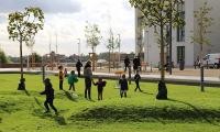 Der Rasen ist teils eine kleine Hügellandschaft. (Foto: Stadt Heidelberg) Kinder spielen auf einer hügeligen Rasenlandschaft, einige Bäume sind zu sehen.