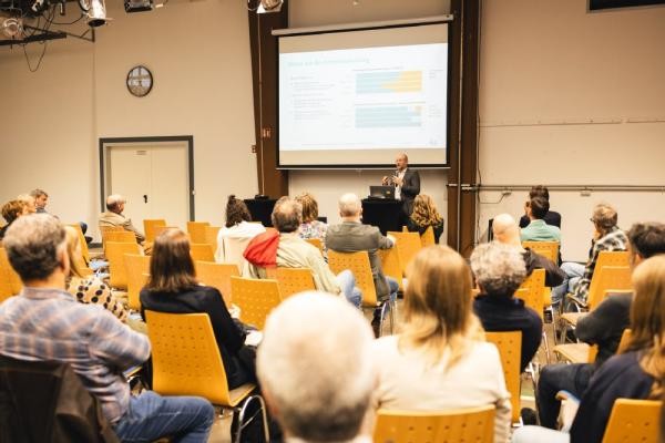 Im Zuge der Veranstaltungsreihe „Stadtentwicklung im Dialog“ fand am Donnerstag, 23. Oktober 2025, im Dezernat 16 der vierte Fachabend zur nachhaltigen Stadtentwicklung statt. (Foto: Hermann Meyer) Eine Gruppe von Menschen sitzt in Reihen und betrachtet vor sich eine Präsentation die von einem Mann gegeben wird