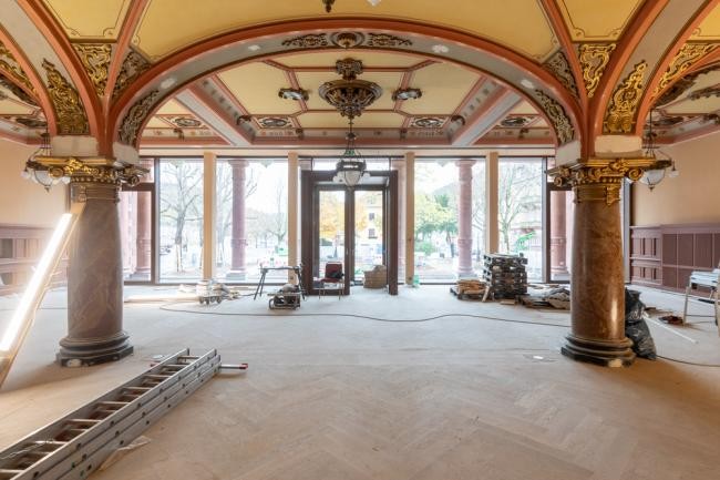 Die Sanierung der Stadthalle befindet sich auf der Zielgeraden – wie auch der Blick in den Meriansaal zeigt. (Foto: Christian Buck) Das Foto zeigt das innere der Stadthalle. Die Decke ist von verzierten Bögen gekennzeichnet und auf dem Boden befinden sich auf dem Parkett noch Bauutensilien, darunter eine Leiter