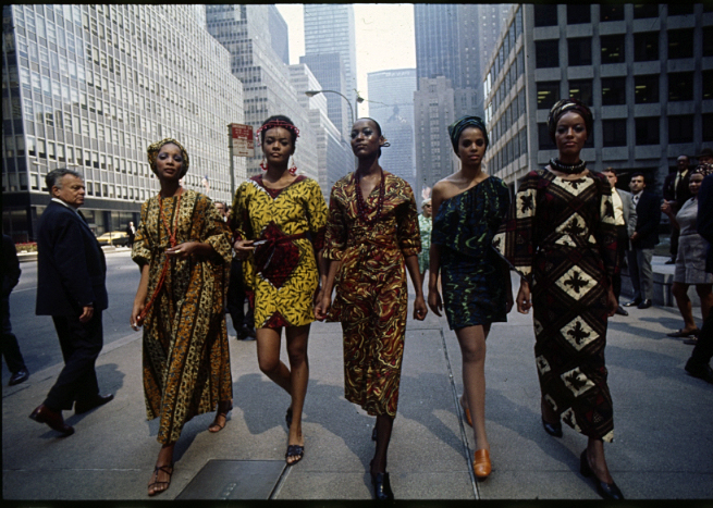 The color photo shows four black female models in colorful dresses made of African fabrics against the Manhattan skyline.