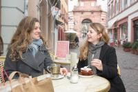 Zwei junge Frauen sitzen draußen und trinken gemeinsam einen Kaffee an einem runden Tisch (Foto: Buck)