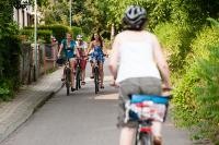 Drei Jugendliche fahren mit dem Fahrrad eine Straße mit viel Grün entlang und lachen. Eine weitere Radfahrerin ist von hinten zu sehen (Foto: Stößer)