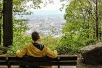 Ein Mann mit gelber Jacke sitzt auf einer Bank im Wald und genießt die Aussicht auf die Stadt (Foto: Stadt Heidelberg/ Pellner)