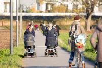 Auf einer Straße laufen zwei Frauen mir einem Kinderwagen. Im Vordergrund ist eine Frau, die ein Fahrrad mit einem Kindersitz schiebt (Foto: Buck)