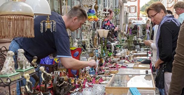 Ein langer Tisch mit vielen alten Dingen, die verkauft werden. Links vom Tisch steht ein Verkäufer und rechts sind Menschen, die sich die Dinge anschauen. (Foto: Rothe)