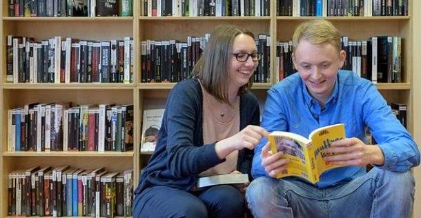 Ein Mädchen und ein Junge sitzen vor einem Bücherregal und lesen in einem Buch (Foto: Rothe)