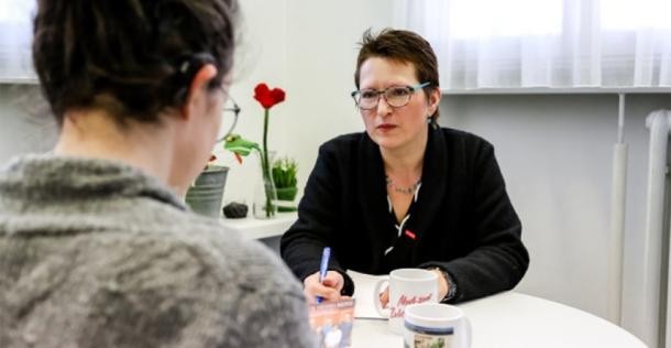 Eine Frau sitzt mit dem Rücken zur Kamera am Tisch, ihr gegenüber die Kommunale Behindertenbeauftragte Christina Reiß