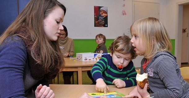 Erzieherin mit zwei kleinen Kindern beim Bilderbuch-Angucken