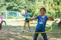 Die Ferien können kommen: In Heidelberg gibt es dank weitreichender Lockerungen durch die Corona-Verordnung in den großen Ferien jede Menge attraktive Angebote für Kinder und Jugendliche. (Foto: Bäcker) Drei Mädchen spielen auf einer Wiese mit Hula Hoop Reifen.
