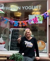 Alexandra Kühner vor ihrem Laden "Yolicious". (Foto: Kühner) Alexandra Kühner sitzt vor ihrem Laden "Yolicious" und hält ein Sektglas in die Höhe.