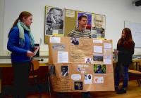Drei Jugendliche präsentieren ein selbstgebasteltes Plakat im Klassenzimmer