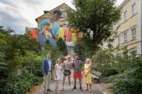 Stellten gemeinsam das neue Wandgemälde in der Plöck vor, das kurz vor der Fertigstellung steht (v.l.): Marc Massoth, Leiter des Amtes für Wirtschaftsförderung und Wissenschaft, Carola Noack, Inhaberin des „Madame Kuvèl“ in der Plöck, Künstler Matthias Mross, Pascal Baumgärtner vom Metropolink Festival und Iris Schiller vom Amt für Wirtschaftsförderung und Wissenschaft. (Foto: Philipp Rothe) Gruppenfoto vor Gemälde