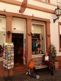 Eine Station bei den Touren ist beispielsweise der Eine-Welt-Laden. (Foto: Stadt Heidelberg) Eine Frau sitzt auf einer Bank vor dem Eine-Welt-Laden.