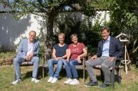 Vier Personen sitzen auf Bänken im Garten