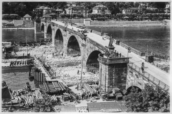 Schwarz-Weiß-Aufnahme der Alten Brücke, mit trockengelegten Pfeilern und viele Baumaterialien am Fuße der Brücke.