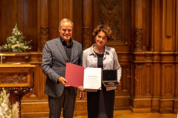 Ein Mann und eine Frau stehen nebeneinander mit der Medaille und einer Urkunde in der Hand