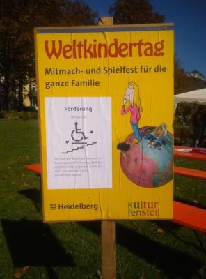 Ein gelbes Schild mit der Aufschrift "Weltkindertag - Mitmach- und Spielefest für die ganze Familie"
