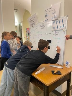Simulationsbrillen im Einsatz (Bild: Stadt Heidelberg) Kinder stehen vor einer Tafel und testen mit den Brillen zu schreiben