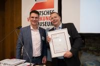 Marc Massoth überreicht Hans-Georg Böcher eine Urkunde zum 25-jährigen Bestehen des Verpackungsmuseums.