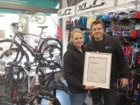 Sabine und Thorsten Kirch in ihrem Laden in der Plöck. (Foto: Stadt Heidelberg) Eine Frau und ein Mann stehen in einem Laden und halten eine Urkunde in den Händen. Im Hintergrund sind Fahrräder zu sehen.