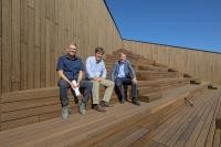 Projektleiter der Bauherrin Bau- und Servicegesellschaft mbH Heidelberg (BSG) Wahid Saberi, Erster Bürgermeister Jürgen Odszuck und Geschäftsführer der städtischen Gesellschaft Heidelberg Congress (HC) Thomas Sante begutachteten bei der Tour durch das ganze Gebäude auch den neunten Seminarraum – eine Besonderheit: unter freiem Himmel, jedoch völlig multimedial ausgestattet. (Foto: Philipp Rothe) Drei Männer sitzen auf einer holzvertäfelten Treppe auf dem Dach des Congress Centers.