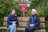 Einladung zum spontanen Plausch: Wer auf einer der neu gekennzeichneten „Plauderbänke“ sitzt, signalisiert, dass er gerne für ein lockeres Gespräch mit anderen Menschen bereit ist. (Foto: Rothe) Zwei Menschen unterhalten sich auf einer Bank.
