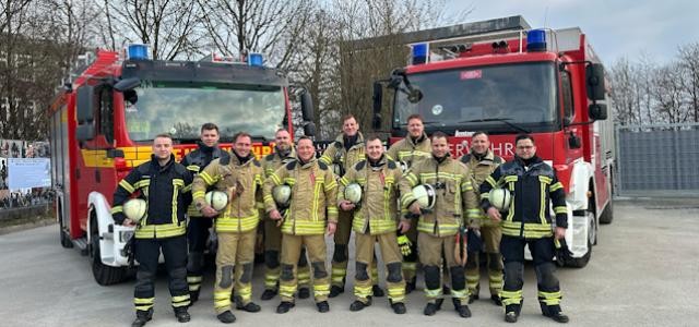 Gruppenbild der Lehrgangsteilnehmer mit Einsatzkleidung, die vor zwei Feuerwehrfahrzeugen stehem