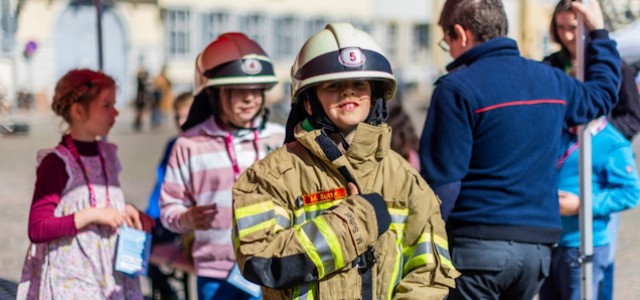 Ein Kind hat eine Feuerwehracke und Helm an und schaut in die Kameras