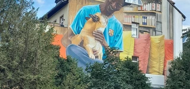 Auf eine Hauswand ist ein buntes Bild gemalt: Ein schwarzer Mann hat einen Hund auf dem Schoß.