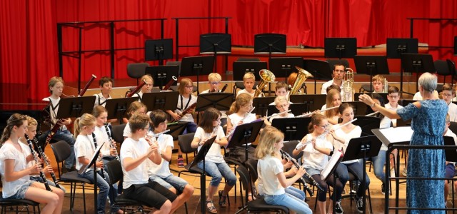 Kinder sitzen mit Instrumenten auf einer Bühne.