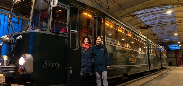 Zwei Frauen stehen vor einer grünen Tram aus den Sechziger Jahren.