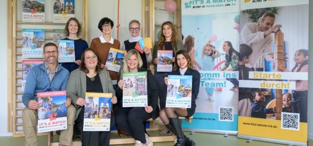 Bürgermeisterin Stefanie Jansen steht mit Myriam Lasso und 6 weiteren Personen vor einer Holzkletterwand für Kinder und neben zwei Werbeaufstellern für It´s a match.
