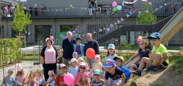 Einige Kinder und Erwachsene in einem Garten vor einem mit Girlanden geschmückten Bau.