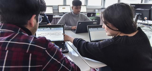 Drei Schüler sitzen vor Laptops und unterhalten sich.
