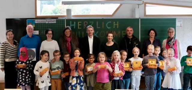 Mehrere Kinder und Erwachsenene stehen vor einer Tafel in einem Klassenzimmer,