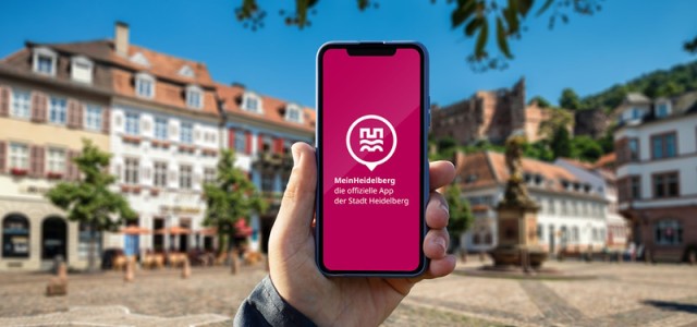 Hochgehaltenes Handy mit der App vor dem Marktplatz