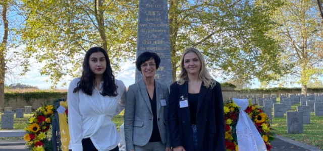 Foto von drei Personen vor einem Denkmal aus Stein.