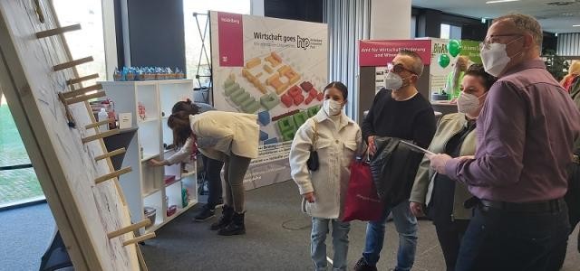 Personen stehen vor einer Wurfwand, auf die Ringe geworfen werden können.