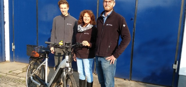 Eine Frau wird von zwei Männern flankiert. Vor ihnen steht ein E-Bike.