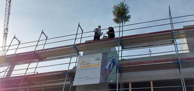 Zwei Handwerker geben den Richtspruch auf dem Gerüst eines Rohbaus vor strahlend blauem Himmel