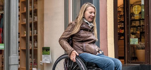 Frau fährt mit Rollstuhl aus Hauseingang
